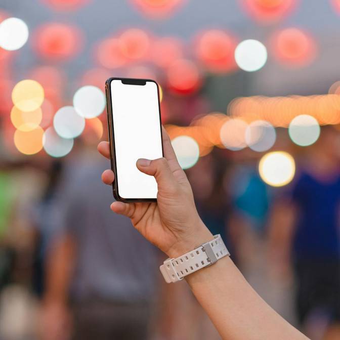 Ein Bild eines iPhones mit weißem Bildschirm, das vor einen verschwommenen Hintergrund gehalten wird.